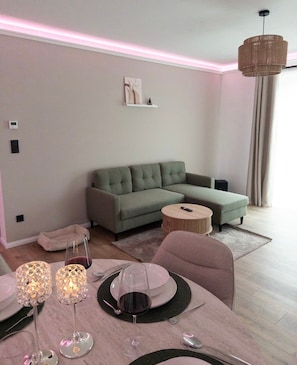 A modern living room with a sectional sofa, a round coffee table, and a dining area set with a table, chairs, and candlelit lamps.