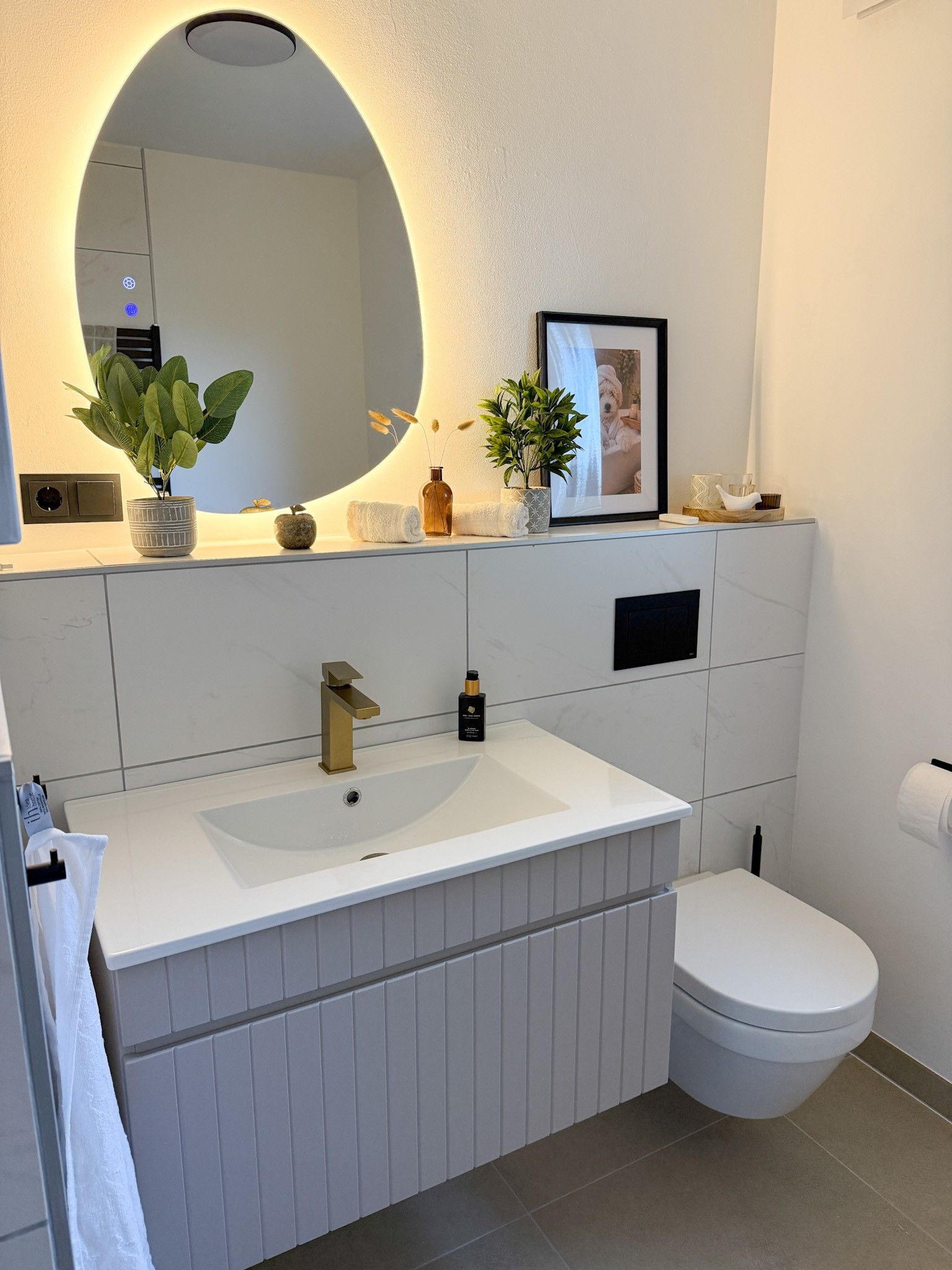 A modern bathroom with a white sink, a toilet, and a large mirror with a circular light.