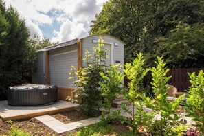A small shed with a door and windows, a hot tub, and a garden with various plants. - Toast Stays - Elsie's Retreat (Durham)
