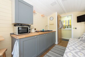 Cozinha compacta com micro-ondas, pia e bancada de madeira.