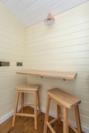 A room with two wooden stools, a wooden shelf, and a ceiling light fixture. - Toast Stays - Elsie's Retreat (Durham)