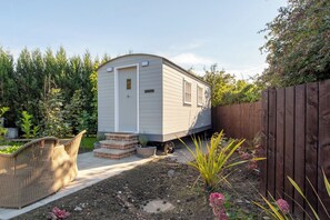 A mobile home with a small porch and steps leading to the door, surrounded by a wooden fence and garden plants. - Toast Stays - Elsie's Retreat (Durham)