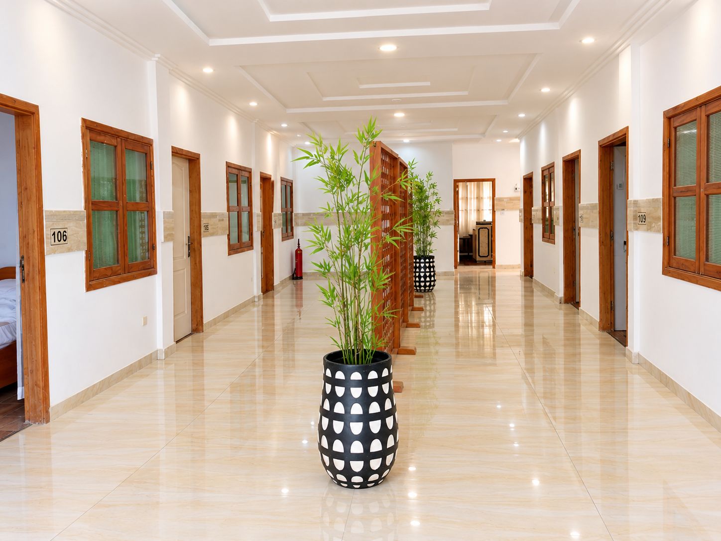 A hotel corridor with a polished floor, wooden doors, and a potted bamboo plant.