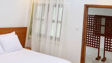 Une chambre à coucher comprenant un lit, un ventilateur de plafond, une fenêtre avec des rideaux légers et une cloison en bois.