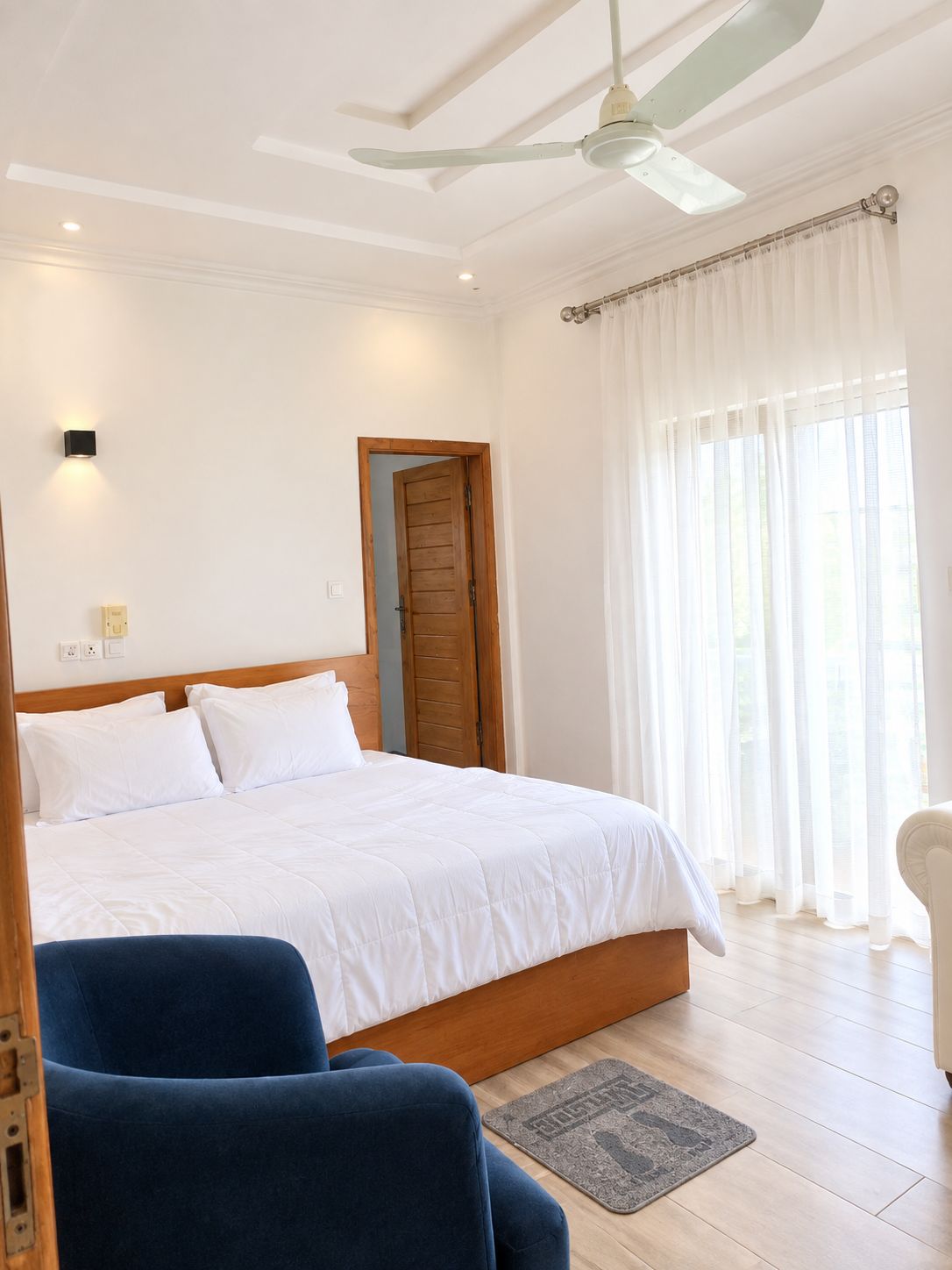 Une chambre à coucher avec un lit, un ventilateur de plafond, une porte en bois et une fenêtre avec des rideaux.