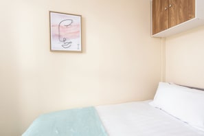 A bedroom with a bed, a light blue blanket, a white pillow, and a wooden wardrobe. - Toast Stays - Number 46 (Hill Top)