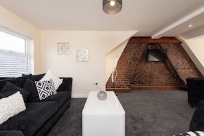 A living room with a black sofa, white cushions, a white coffee table, and a brick fireplace. - Toast Stays - Number 46 (Hill Top)