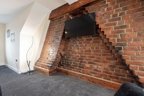 A room with a brick fireplace, a flat-screen TV mounted on the wall, and a carpeted floor. - Toast Stays - Number 46 (Hill Top)