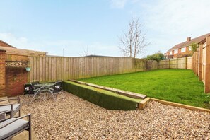 A backyard with a wooden fence, a grassy lawn, and a gravel area with outdoor furniture. - Toast Stays - The Pittington Loft (High Pittington)