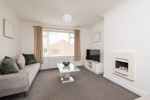 A living room with a sofa, a coffee table, a television, and a fireplace. - Toast Stays - The Pittington Loft (High Pittington)