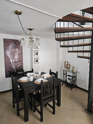 A dining area with a wooden table set for four, surrounded by dark wooden chairs. A chandelier hangs from the ceiling, and a spiral staircase is visible in the background. - New Listing (Medellín)