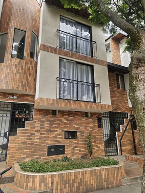 A multi-story residential building with brick facade, balconies, and a small garden area. - New Listing (Medellín)