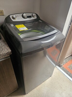 A front-loading washer and dryer unit with a control panel, placed in a corner with a granite countertop and a wooden cabinet. - New Listing (Medellín)