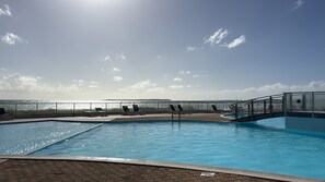Una piscina amb gandules i una barana de vidre amb vista al mar.