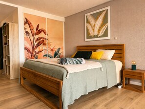 Un dormitori amb un llit de fusta, una manta de punt verd i un mural amb plantes tropicals.