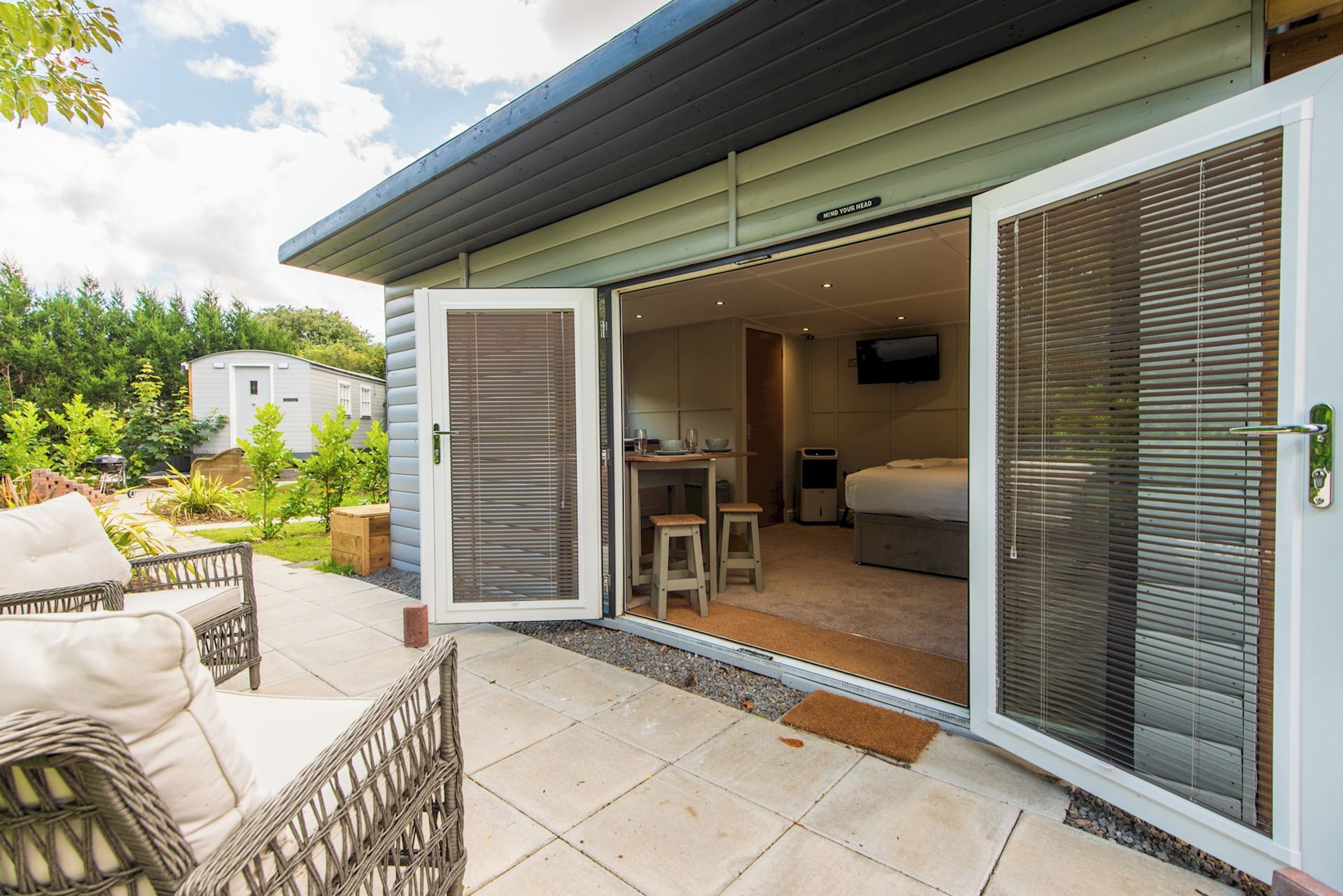 A modern house with a patio, a dining area, and a bedroom visible through an open sliding door.