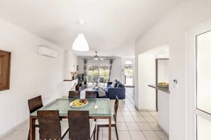 A dining area with a glass table, chairs, and a plate of fruit. There is a kitchen in the background with a TV and a dining table. - Villa Lilly Rose - Three Bedroom Villa, Sleeps 6 (Polis)