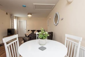 A dining area with a round table, chairs, a vase with flowers, and a small electronic device on the table. - Toast Stays - The Langley Nook (Hill Top)