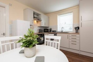 A modern kitchen with white cabinetry, a dining table with chairs, and a potted plant. - Toast Stays - The Langley Nook (Hill Top)