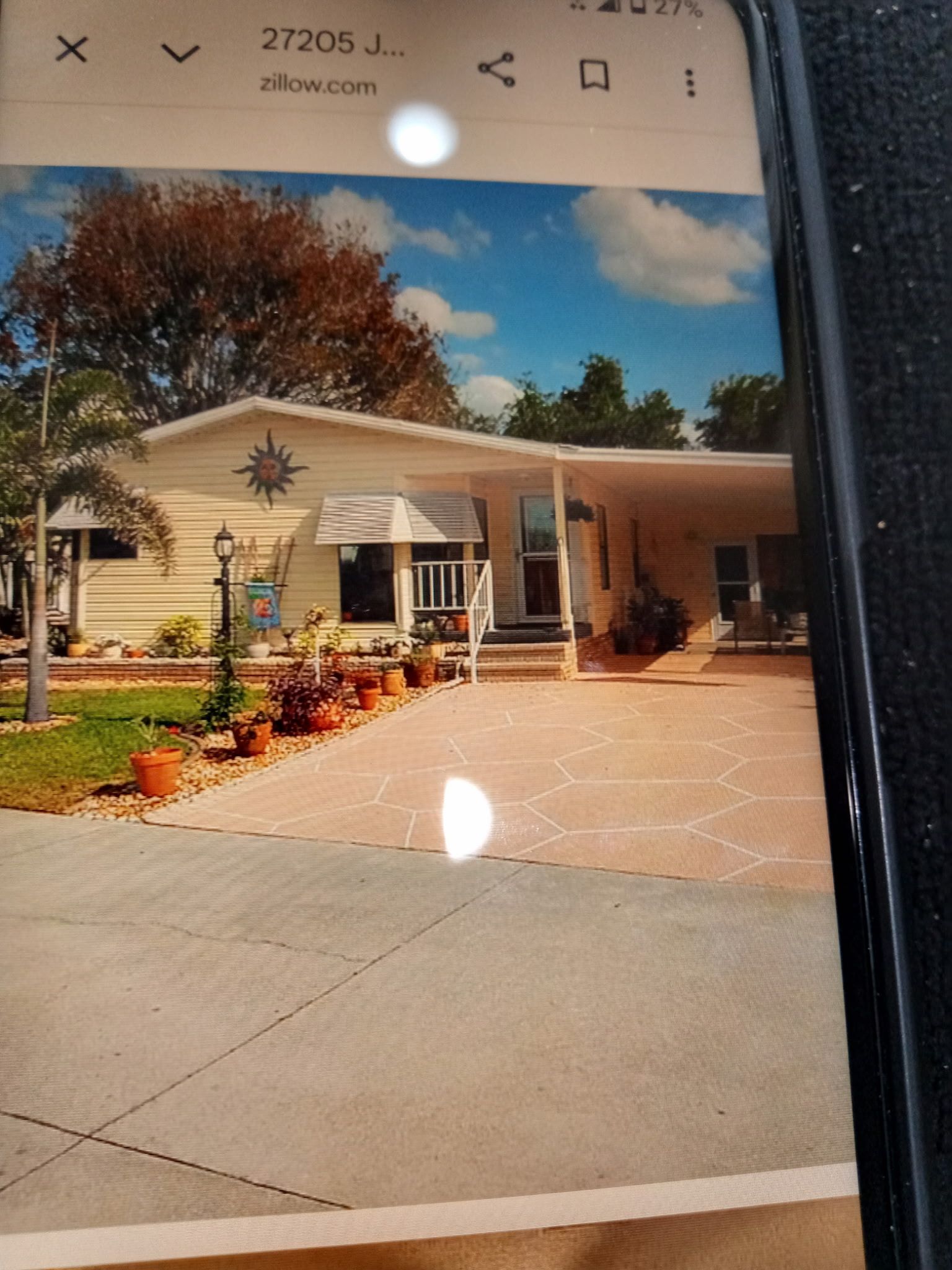 A single-story house with a covered porch, a front yard with potted plants, and a clear sky.