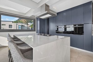 Cocina moderna con una isla grande, muebles oscuros y vistas a una zona residencial.