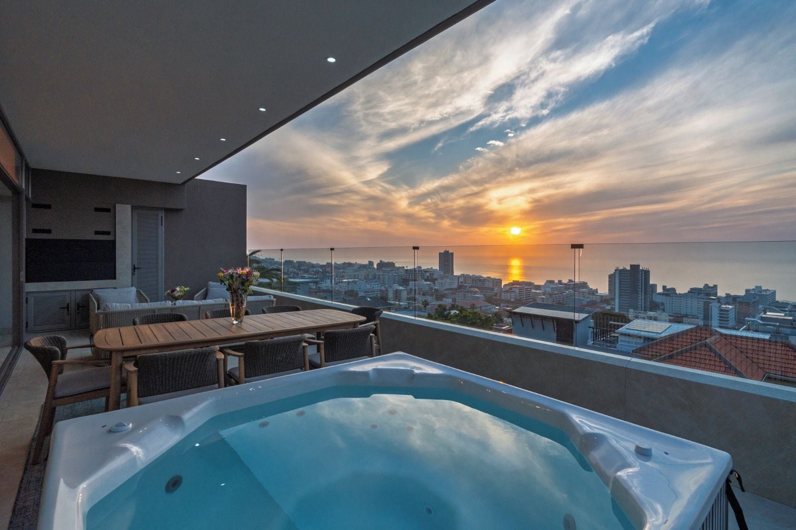 Una terraza en la azotea con un jacuzzi, zona de estar y vistas a la ciudad al atardecer.