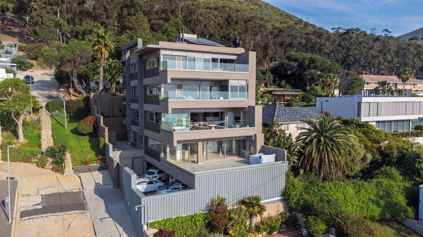 Un edificio residencial de varios pisos con terraza en la azotea, rodeado de abundante vegetación y colinas.