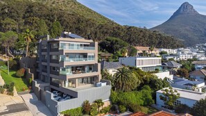 Un edificio residencial de varios pisos con balcones, rodeado de vegetación y una montaña al fondo.