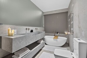 A modern bathroom with a freestanding bathtub, a large vanity with a mirror, and a toilet. - 16 Clifford Rd (Cape Town)