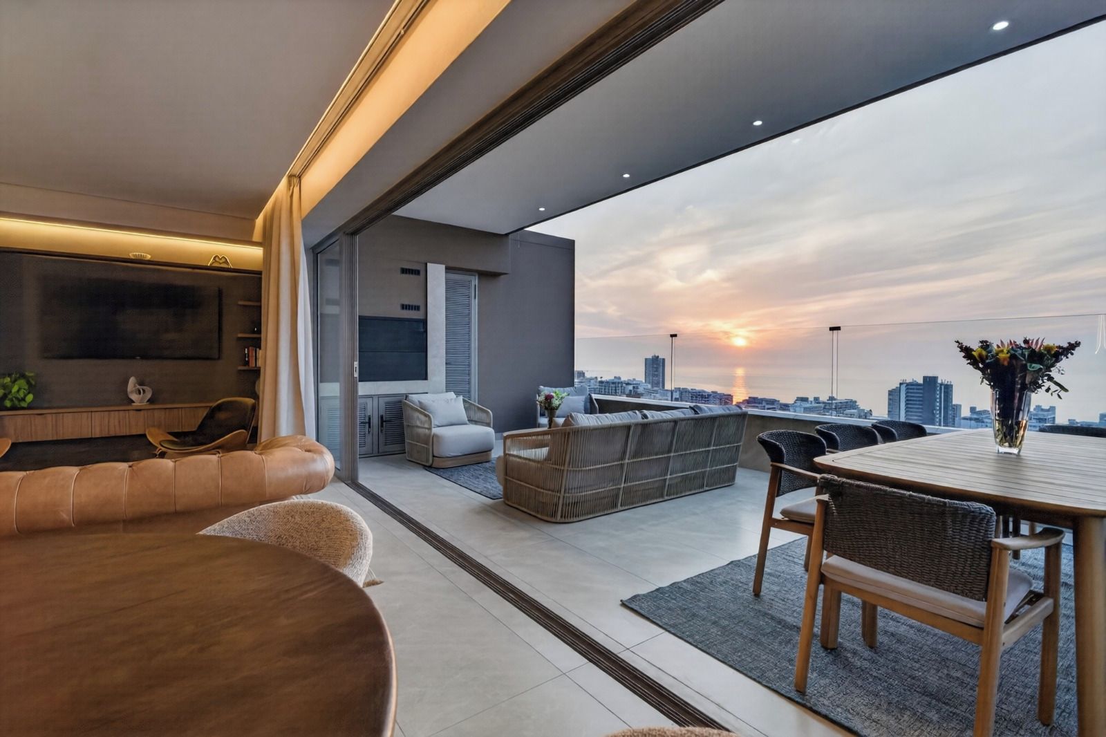 A modern living room with a city view, a flat-screen TV, and a dining area with a table and chairs.