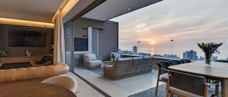 A modern living room with a city view, a flat-screen TV, and a dining area with a table and chairs.
