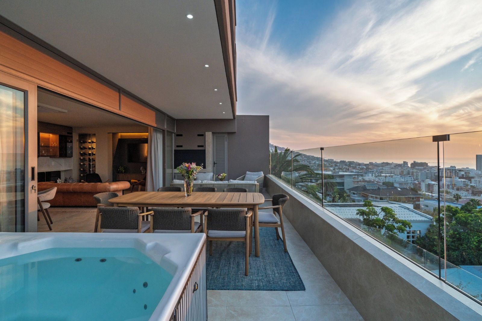 Un balcón moderno con jacuzzi, zona de estar y vistas a la ciudad.