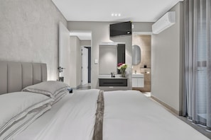 A modern bedroom with a large bed, a bedside table, a built-in TV, and a bathroom with a mirror and sink. - 16 Clifford Rd (Cape Town)