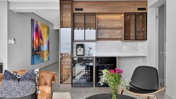 A modern living room with a sofa, a coffee table, and a chair. There is a painting on the wall and a vase with flowers on the table.