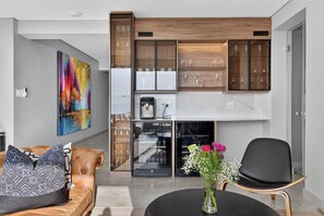 Una sala moderna con un sofá, una mesa de centro y una silla. Hay un cuadro en la pared y un florero con flores sobre la mesa.