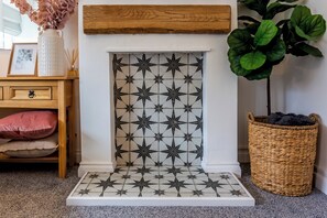A fireplace with a geometric tile pattern, a wooden mantel, a woven basket, and a plant. - Toast Stays - Pleasant View House (Crook)