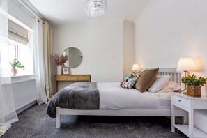 A modern bedroom with a bed, bedside tables, a dresser, a mirror, and a window with curtains. - Toast Stays - Pleasant View House (Crook)