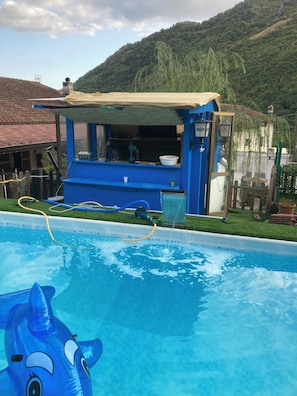 A swimming pool with a blue inflatable shark toy, a blue and beige structure with a window, and a green hillside in the background. - countryside villa with pool quads next near beach mountains rome naples by train (Lazio)