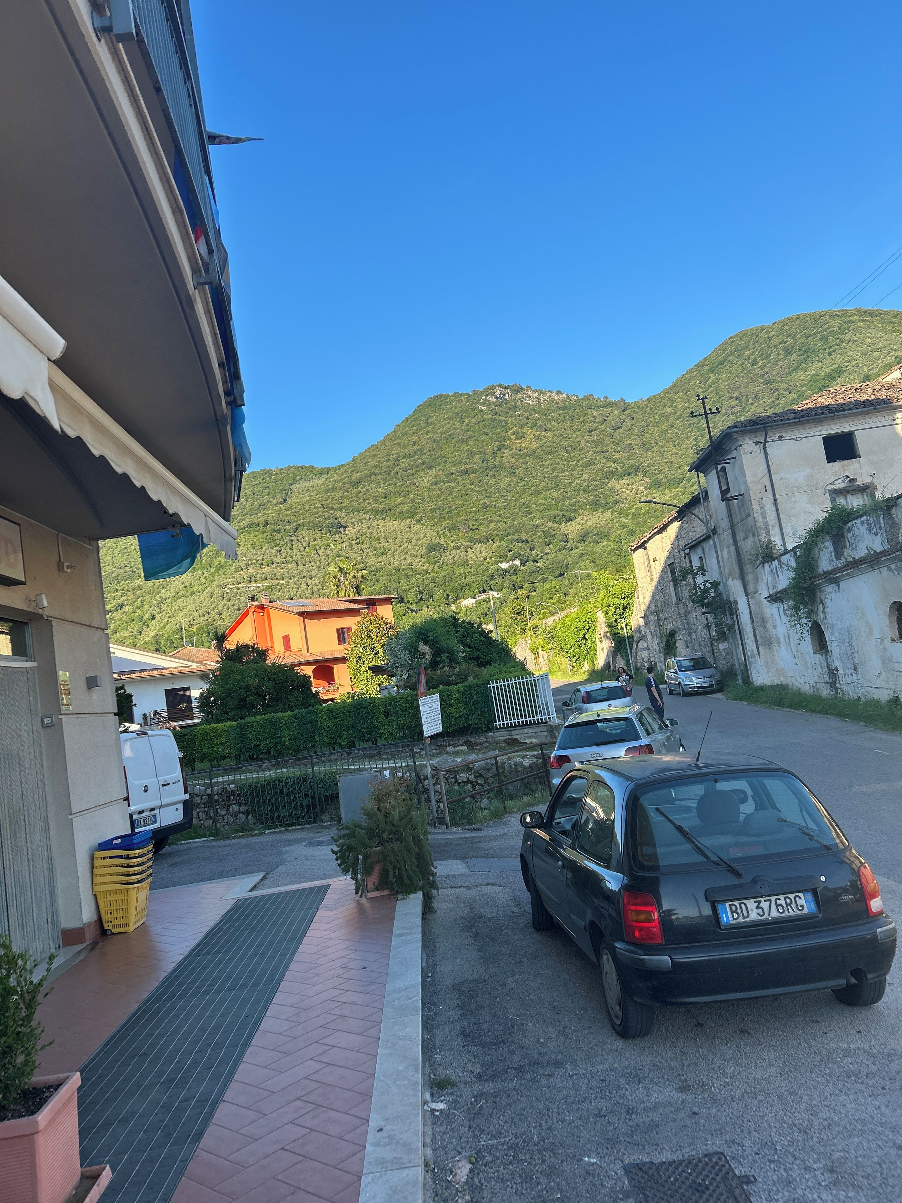 Une rue résidentielle bordée de voitures garées, un immeuble avec un toit en pente et un paysage montagneux en arrière-plan.