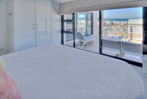 A hotel room with a large bed, a balcony with a view of the city, and a sliding door to the outside. - Charming 2-bedroom apartment in Big Bay near top spots (Cape Town)