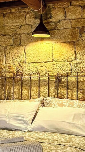 A bed with white linens in a room with stone walls and a hanging light fixture. - La Cicala (Rosignano Marittimo)