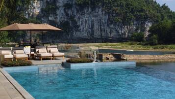 A pool area with lounge chairs and an umbrella, surrounded by a natural landscape with cliffs.