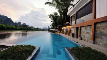 A modern hotel with a swimming pool, stone walls, and a view of a river and mountains.