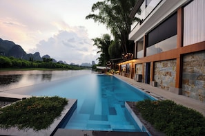A modern hotel with a swimming pool, stone walls, and a view of a river and mountains. - Riverside Paradise Luxury Resort Villa (Guilin)