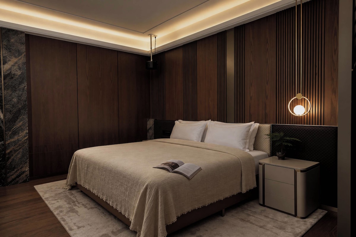 A modern bedroom with a large bed, bedside tables, and a wall-mounted light fixture.