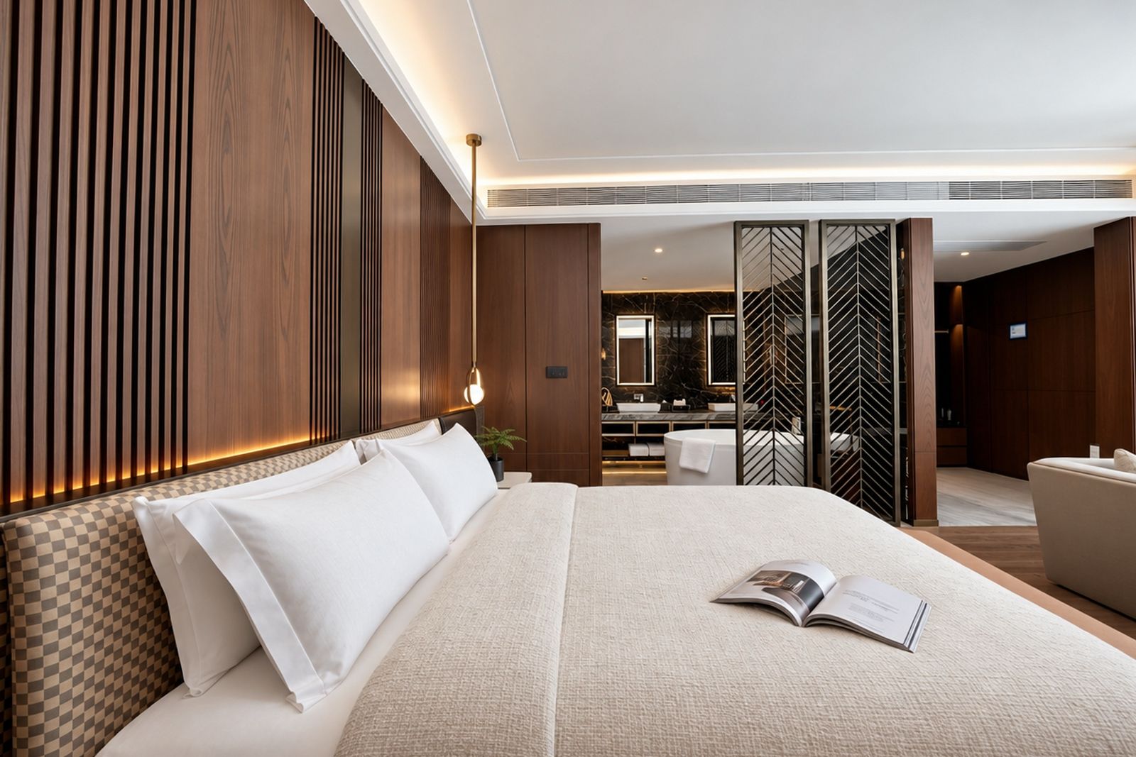Habitación de hotel moderna con una cama grande, una mesita de noche, un rincón de lectura y vistas al baño.