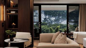 A modern living room with a sofa, armchairs, a small round table, and a large window offering a view of a forested mountain.