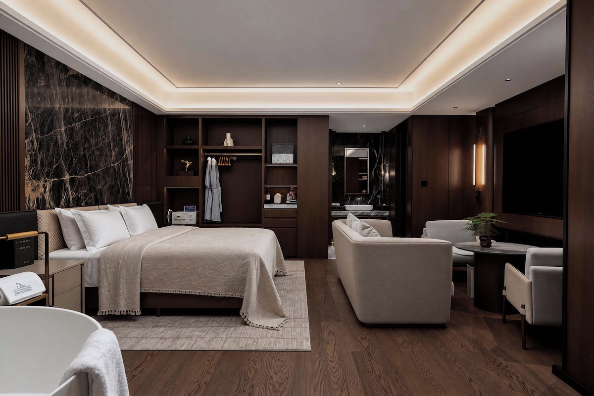 A modern hotel room with a bed, seating area, and a television.