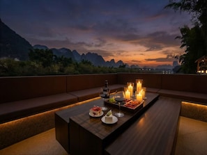 A sunset view from a rooftop terrace with seating and a table set for a meal. - Riverside Paradise Luxury Resort Villa (Guilin)