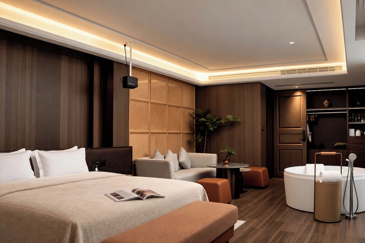 A modern hotel room with a large bed, a sofa, a small table, and a round seating area.